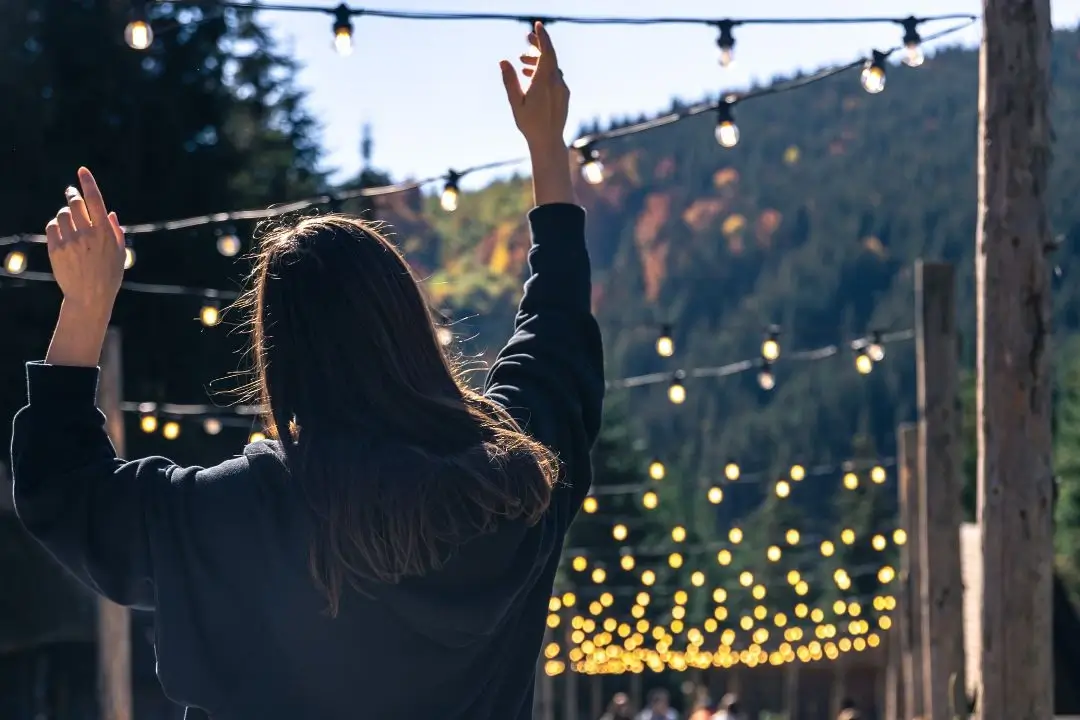 Woman reaching towards outdoor string lights.