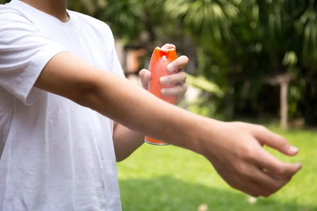 Person applying sunscreen on arm outdoors.