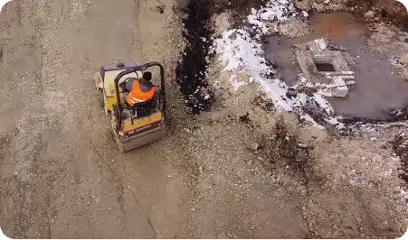 A man driving a road roller on a dirt road.
