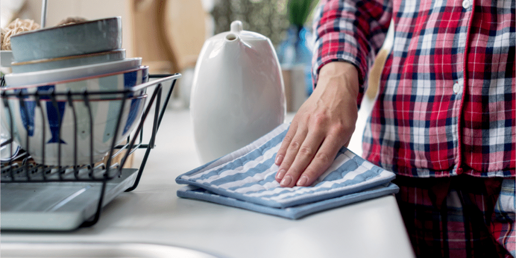 Hand wiping a countertop with a blue cloth near dishes.