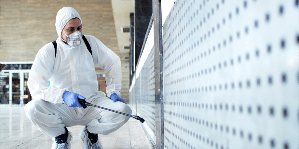 Worker in protective gear spraying for pests indoors.